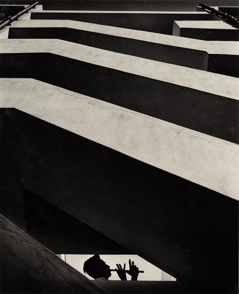 Looking up through concrete balconies at a figure playing a flute