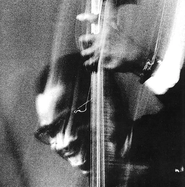 A blurred black-and-white photograph of a musician playing an upright bass